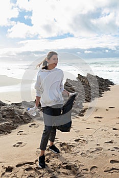 Earth day. Young female activist putting plastic bottles in a garbage bag, cleaning coastal zone, cropped, vertical shot