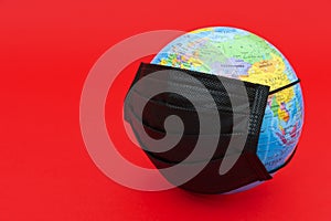 Earth globe model with black surgical mask isolated on red background.