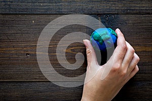 Earth. Hand hold plastiline symbol of planet Earth globe on dark wooden background top view copy space