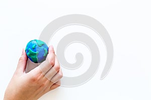 Earth. Hand hold plastiline symbol of planet Earth globe on white background top view copy space
