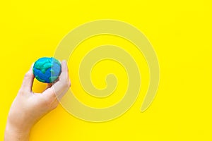 Earth. Hand hold plastiline symbol of planet Earth globe on yellow background top view space for text