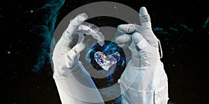 Earth heart in astronaut hands in space background, among stars and galaxies