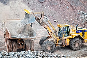 Earth mover loading a dumper truck with porphyry rocks in a mine