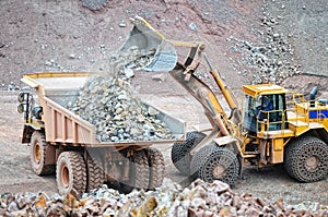 Earth mover loading dumper truck with rocks in quarry