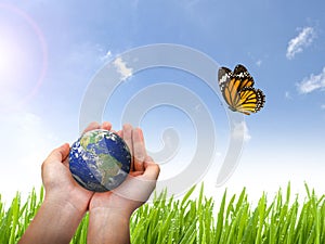 Earth planet and butterfly in female hand on blue sky