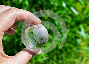 Crystal globe in the hand of a man against a background of green foliage. Earth protection concept. Earth Day