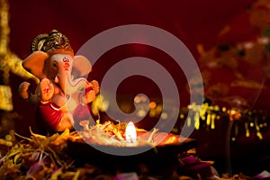 Earthen lamp on rose petals with ganesha statue over the blurry red golden background. hinduism concept