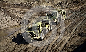 Earthmoving vehicles following each other while scrapping dirt