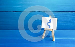 An easel with a curved arrow avoiding an obstacle. Deviation from route, side mission. Maneuvering, taking right action. photo
