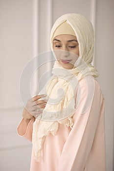 East girl in a beautiful bright Muslim dress, a shawl on her head on a light classical background