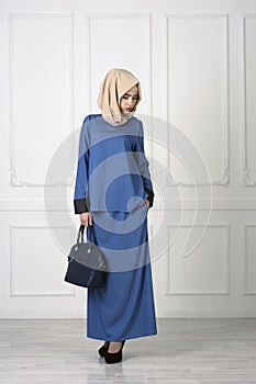 East girl in a beautiful bright Muslim dress, a shawl on her head on a light classical background