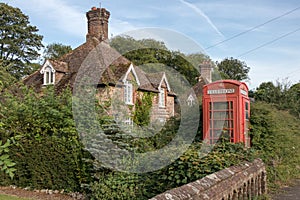 Red public telephone box in garden of Old idilic country brick cottage in chocolate box touristic setting