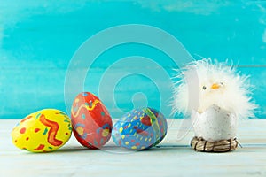 Easter baby chicken next to eggs on blue wooden background