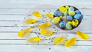 Easter background with a basket and Easter blue and yellow eggs and tulip petals on a light wooden background. photo