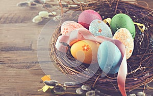 Easter background. Beautiful colorful eggs in nest with spring flowers over wood