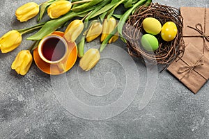 Easter background with blue, green eggs and a cup of tea in nest and yellow tulips. Top view