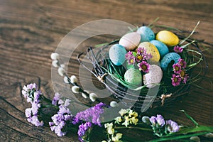 Easter background. Bright colorful eggs in nest with spring flowers over wooden dark background. Selective focus with