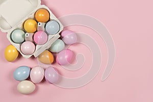 Easter background with a carton egg box with pastel colored easter eggs in and beside it on a pink background with space for copy