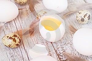 easter background with chicken quail one broken eggs and feathers on white wooden table, food top view