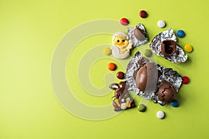 Easter background from chocolate Easter eggs and colorful candies on a green backdrop. Top view and copy space