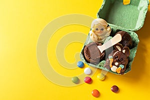 Easter background from chocolate Easter eggs and colorful candies on a yellow backdrop. Top view and copy space