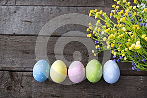 Easter background with colorful eggs and flowers over wood.