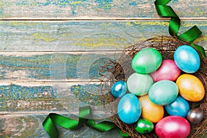 Easter background with colorful eggs in nest decorated with green satin ribbon. Copy space for greeting text. Top view.