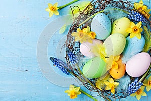Easter background with colorful eggs in nest, feather and spring flowers top view. Holiday card or banner