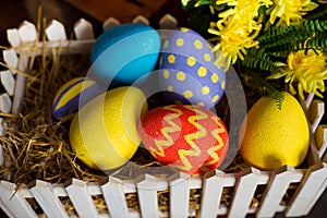 Easter background with colorful eggs, white bunny and yellow flowers over old wood.