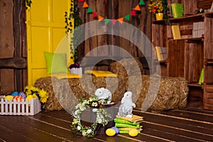 Easter background with colorful eggs, white bunny and yellow flowers over old wood.