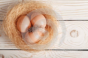 Easter background. Easter beige eggs and feather in nest on rustic white wooden background. Top view, copy space