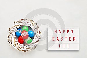 Easter background. HAPPY EASTER written in light box and colorful Easter eggs in wreath on light background. Top view, copy space