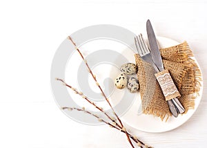 Easter background. Table setting for the holiday of Easter in a rustic style,burlap napkin, quail eggs, fork and knife on a white