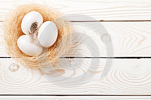 Easter background. Easter white eggs and feather in nest on rustic white wooden background. Top view, copy space