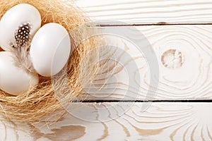 Easter background. Easter white eggs and feather in nest on rustic white wooden background. Top view, copy space