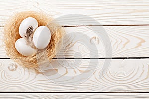 Easter background. Easter white eggs and feather in nest on rustic white wooden background. Top view, copy space