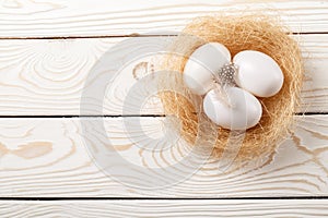 Easter background. Easter white eggs and feather in nest on rustic white wooden background. Top view, copy space