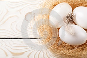 Easter background. Easter white eggs and feather in nest on rustic white wooden background. Top view, copy space