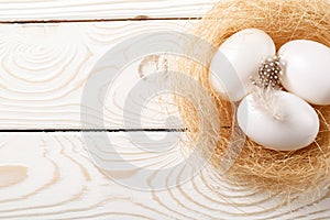 Easter background. Easter white eggs and feather in nest on rustic white wooden background. Top view, copy space