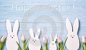 Easter background with white rabbits, pink tulips and text Happy Easter on wooden background, top view