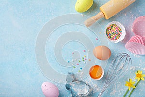 Easter baking background with rolling pin, whisk, eggs, flour and colorful confetti on blue table top view. Flat lay