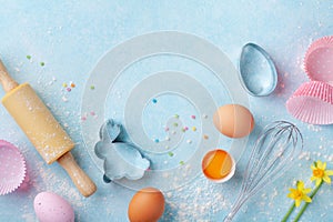 Easter baking background with rolling pin, whisk, eggs, flour and colorful confetti on blue table top view. Flat lay