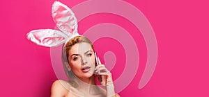 Easter banner with bunny woman. Easter woman with rabbit ears talking on phone,  on pink.