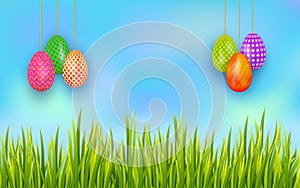 Easter banner with set of colorful hanging eggs and copy space on background with blue sky and grass.