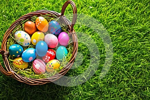 Easter basket with colorful eggs on green grass background. Top view