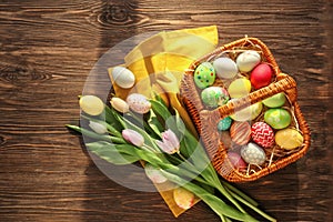 Easter basket with colorful eggs and spring flowers on wooden background, top view