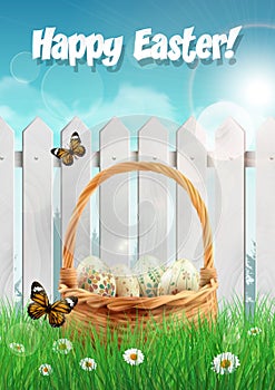 Easter basket with Easter eggs on a field with white picket fence