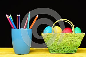 Easter basket full of colourful eggs and mug with pencils