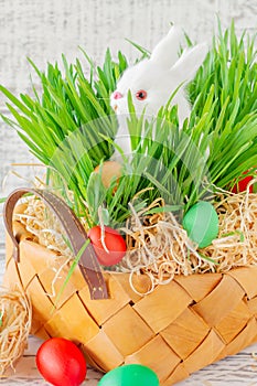 Easter basket with green grass filled with brightly colored Easter eggs and White little bunny. Happy Easter