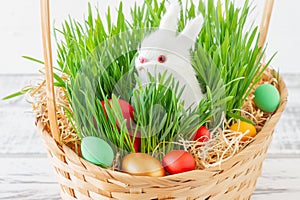 Easter basket with green grass filled with brightly colored Easter eggs and White little bunny. Happy Easter